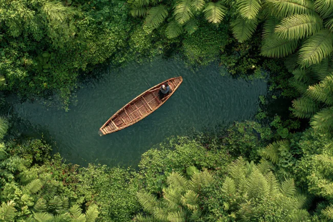 Veneajelu - A serene view of a traditional boat gliding through lush greenery on a tranquil waterway.