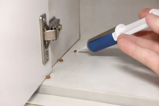 Applying gel bait inside kitchen cabinet